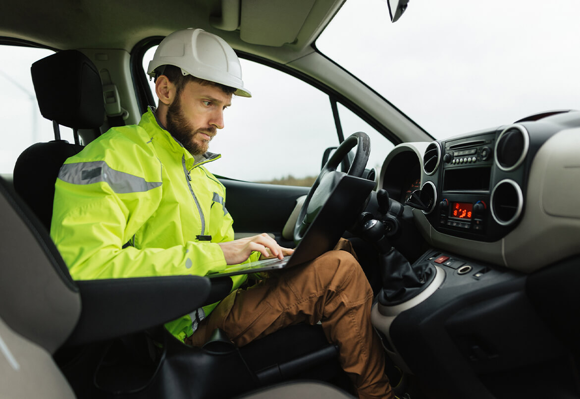 Man in safety gear using a laptop inside a parked car.