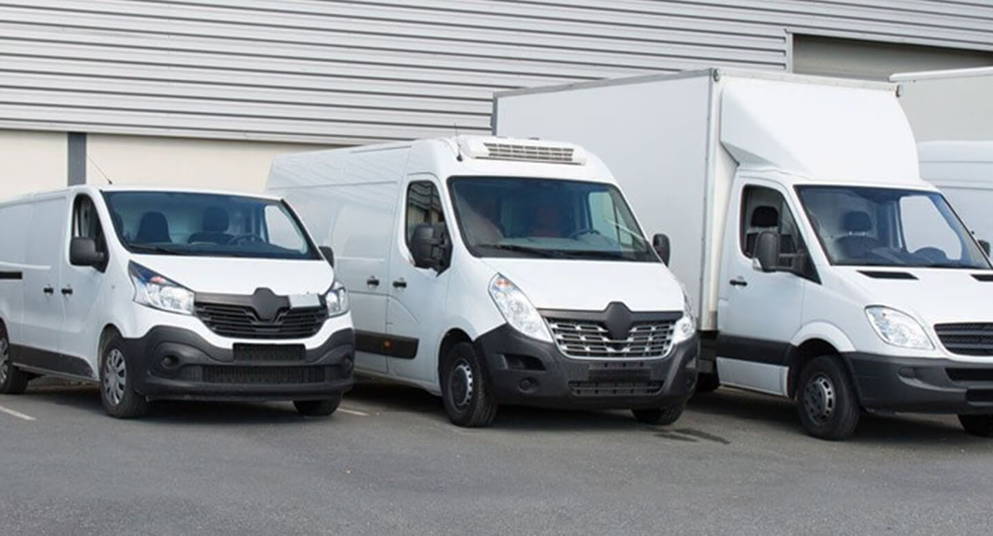 Three white commercial vans parked side by side in an outdoor setting near a building.